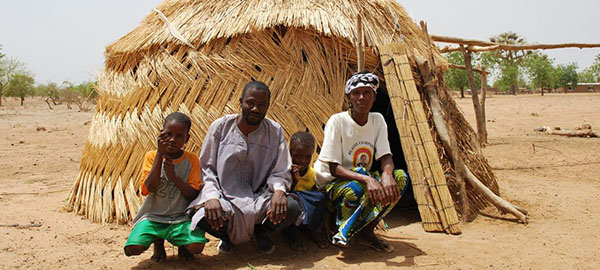 A family sits outside of a straw hut
