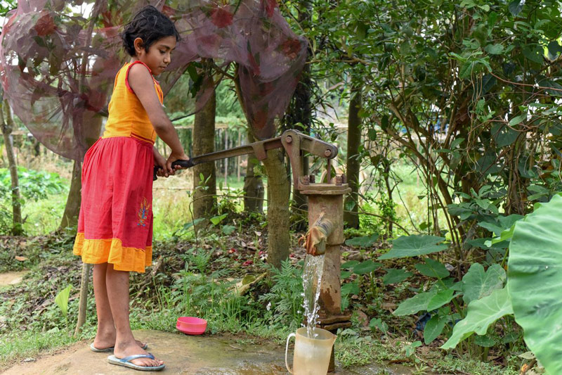 A young girl wearing a colorful dress pumps water from a well
