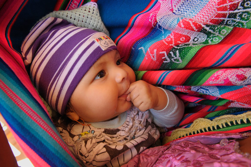 A Bolivian baby is wrapped in traditional, striped fabric