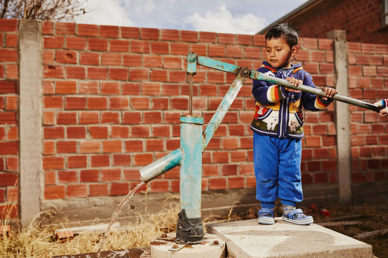 A young boy pumps water from a well