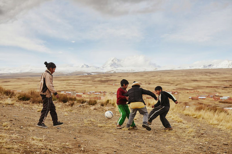 Children play soccer with snowcapped mountains in the distance