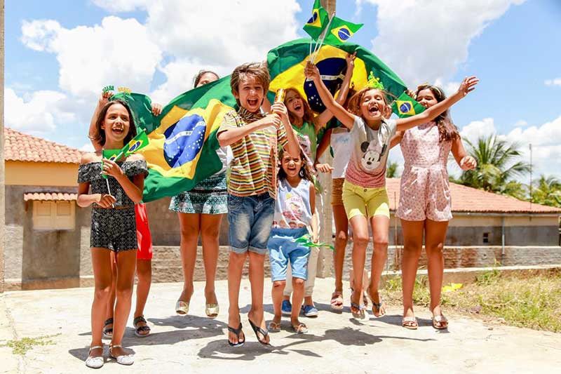 A group of children smile and cheer while holding Brazilian flags
