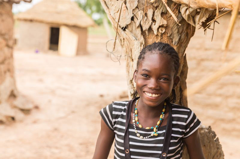 A girl smiles while leaning against a tree in her neighborhood