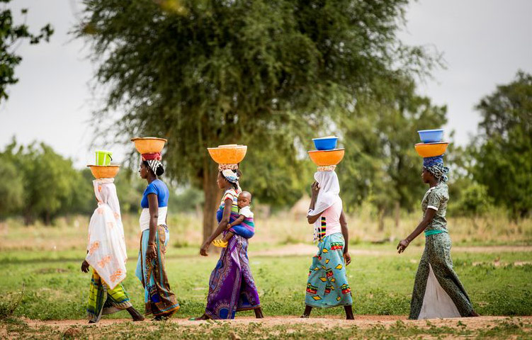 Women carry large bowls of milk on their heads to sell at the market