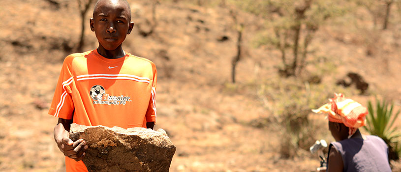 A teenager in an orange shirt is carrying a large rock