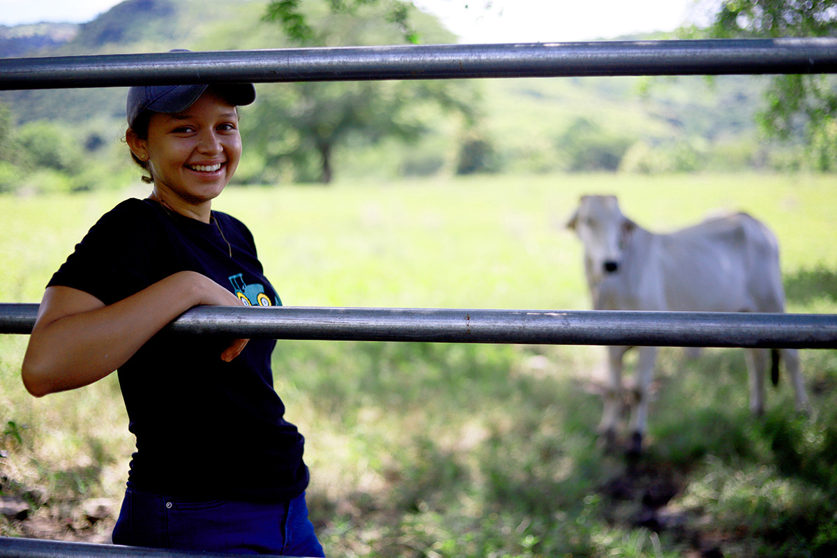 Karina is smiling as she stands at the entrance gate to the field where her cows graze