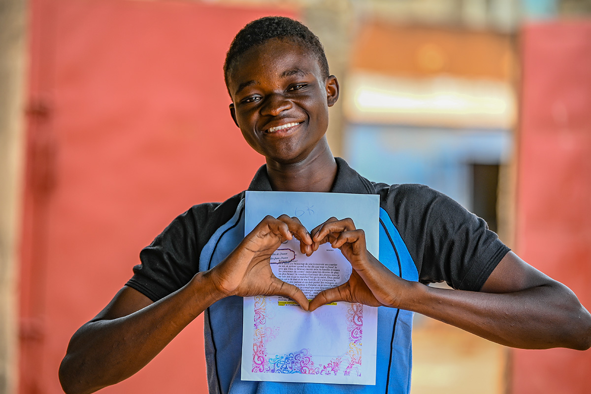Boy holding letter in front of him doing the heart in the middle of the letter with his hands