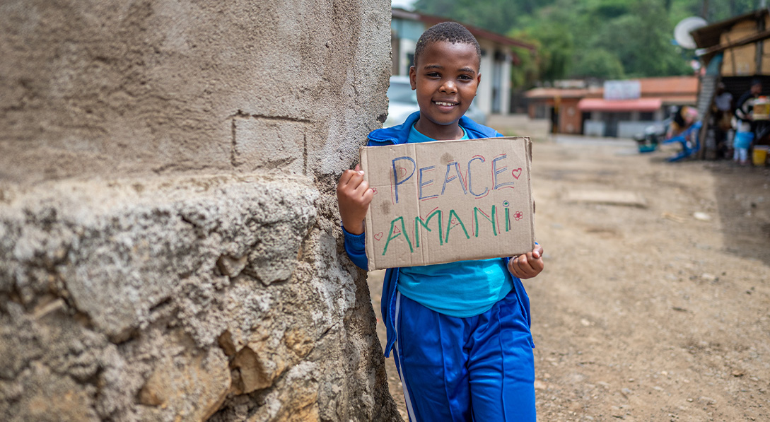 Dorcas holds sign that says "peace" in Swahili