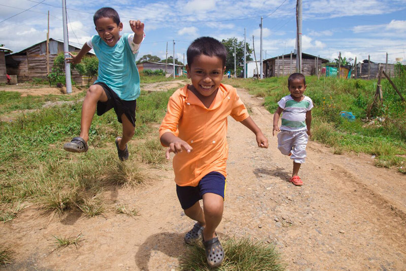 Three brothers from northern Colombia smile as they run down a dirt road