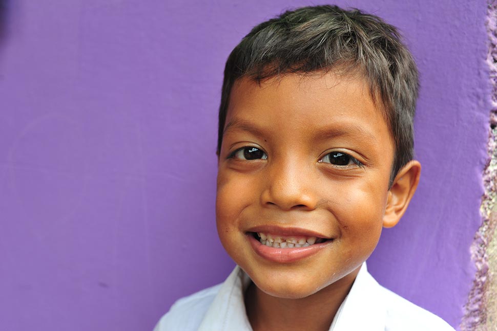 A smiling young boy stands in front of a purple wall