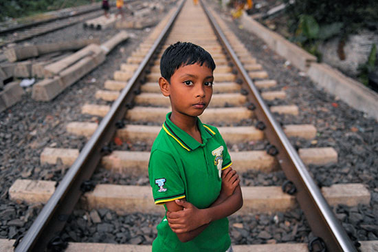 A young Indian boy stands in the middle of some train tracks.