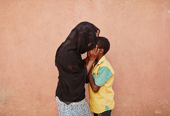 A boy and a woman wearing a black head press their foreheads against one another