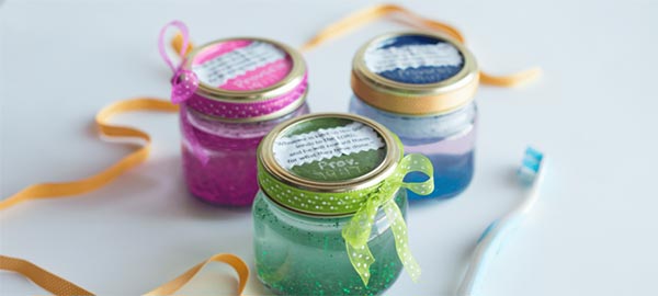 Three small mason jars with ribbon around the lids and different color homemade glitter toothpaste in them
