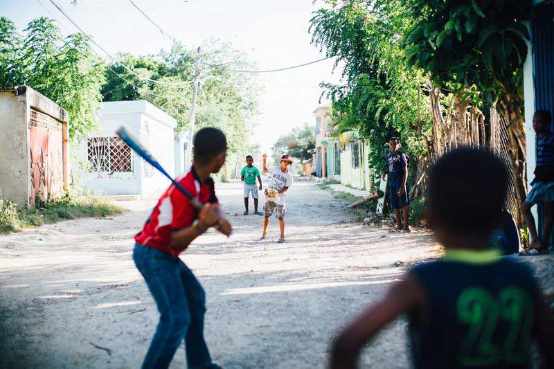 A group of children play baseball in the street
