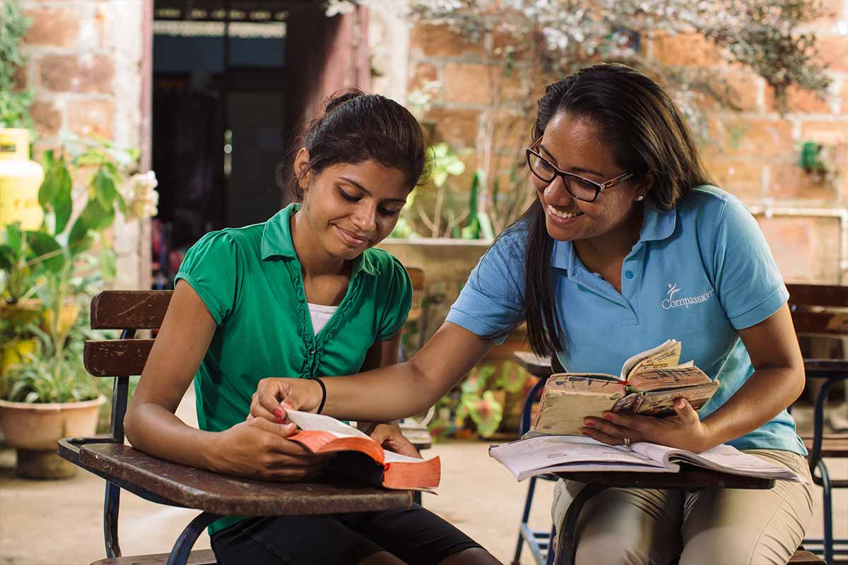 A young teenage girl sits with a Compassion worker and receives tutoring
