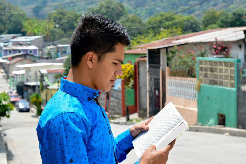 A teenager reads the Bible in his neighborhood