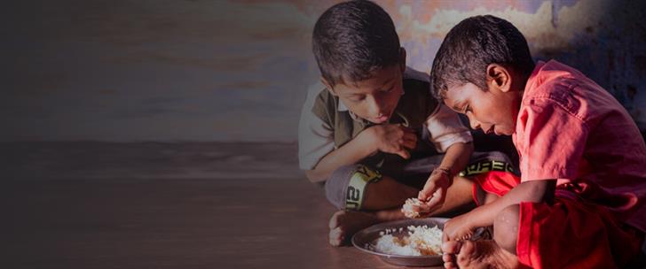 two boys eat rice from a plate with their hands
