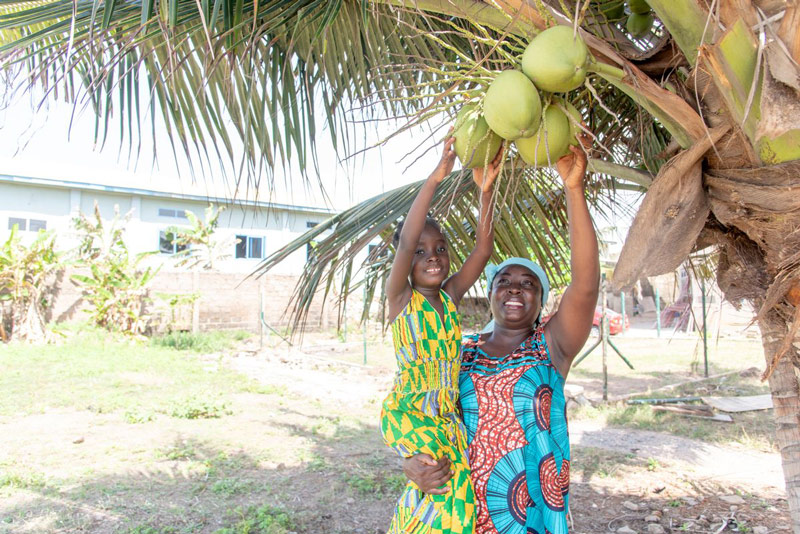 A girl and her mother smile as they reach for a coconut