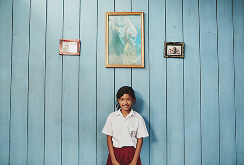 girl in a school uniform in front of a blue wall with framed pictures
