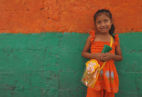 Girl in an orange dress smiling in front of an orange and green wall