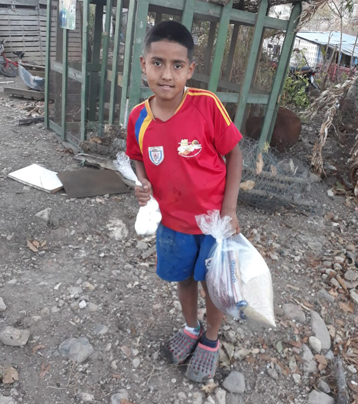a boy stands and smiles with a bag of goods