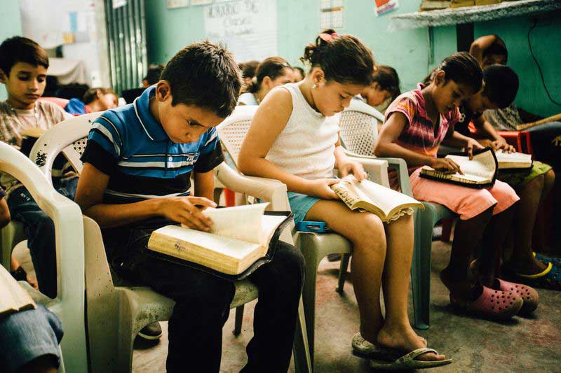 Children sit in a classroom and read their Bibles together