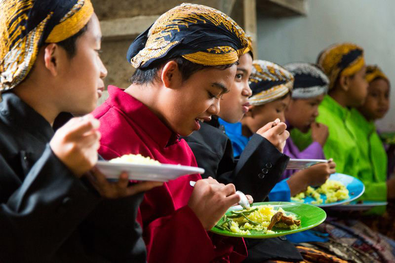 A group of children wearing traditional Indonesian dress have lunch together