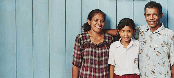 A mother, father and daughter stand in front of a blue wall with three pictures hanging on it.