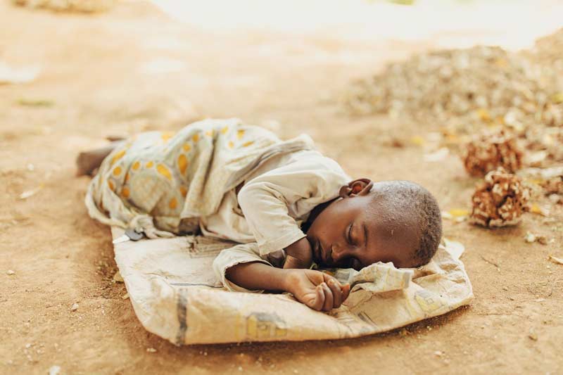 A young child sleeps peacefully on top of an empty burlap sack