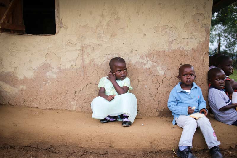 Children sit against the wall of a home