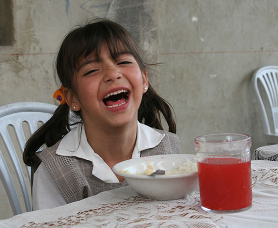 A young girl laughing while eating her meal