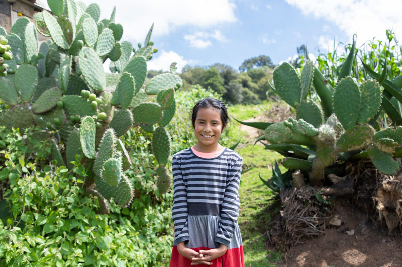 A girl stands in front of cactus and smiles