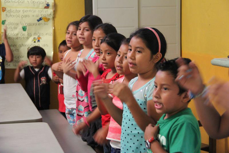 Children stand singing and clapping in class