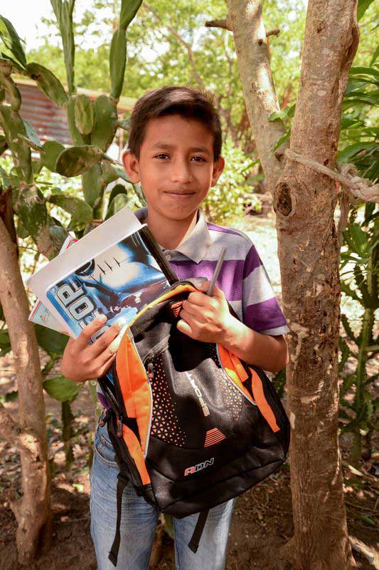 A young boy holds his schoolbooks and backpack in his hands