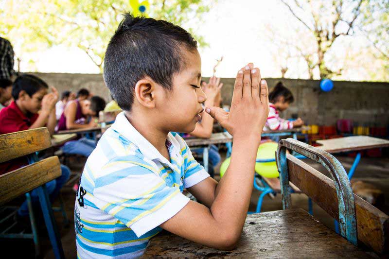 A young boy holds his hands together to pray during a lesson