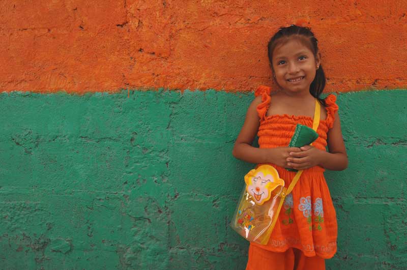 A young girl smiles in front of a colorful wall