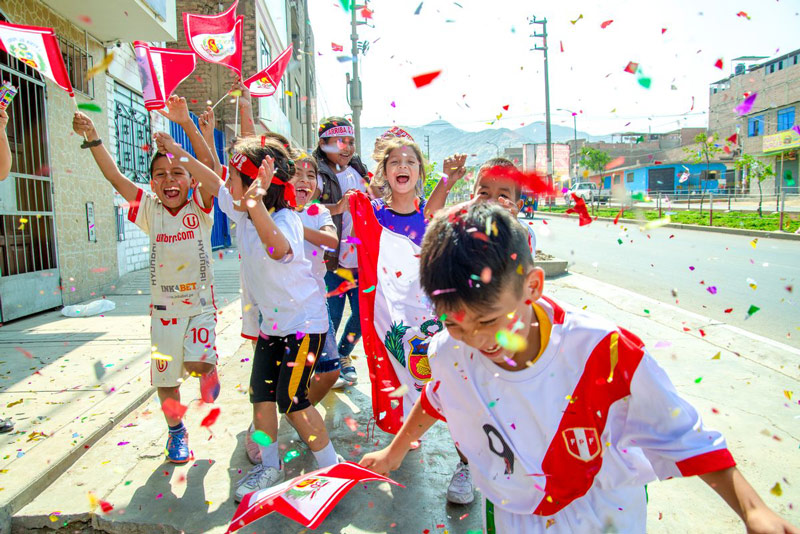 A group of children run through their neighborhood with confetti and Peruvian flags