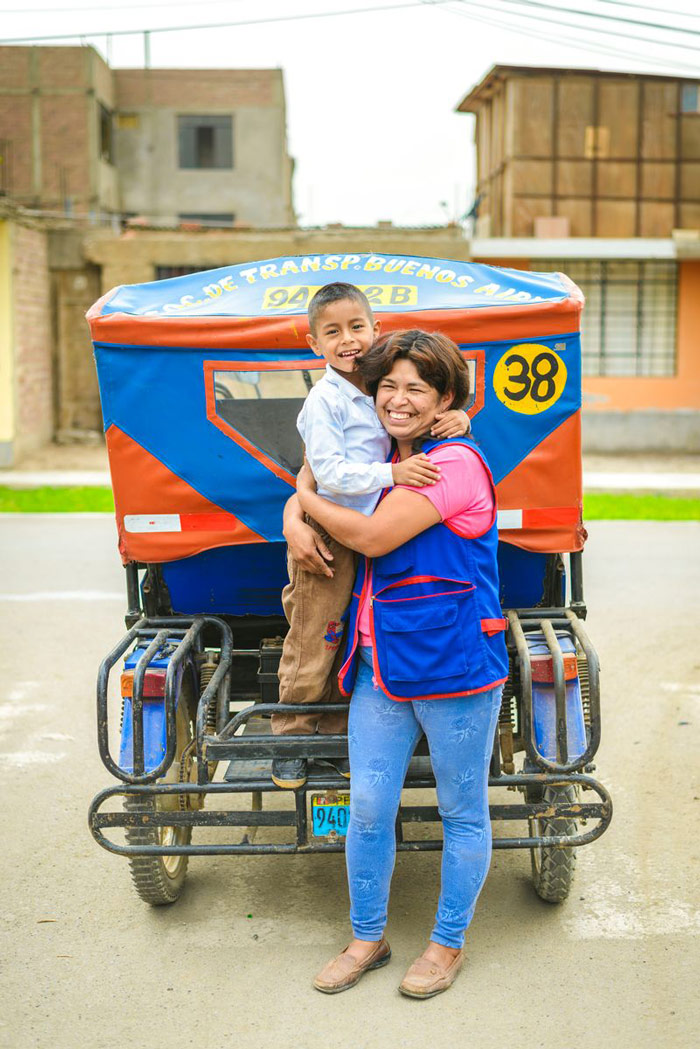 A boy and his mother stand near her red and blue taxi