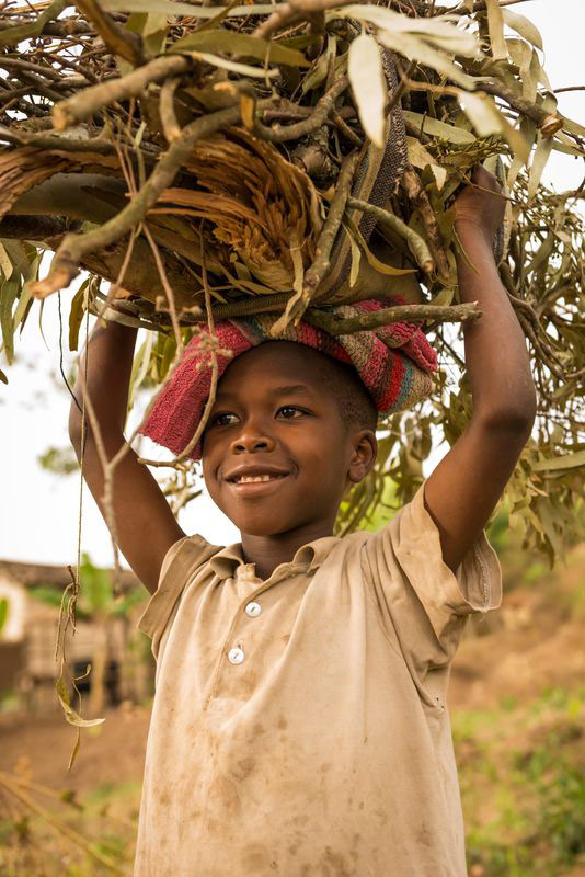 A child carries twigs on her head and smiles