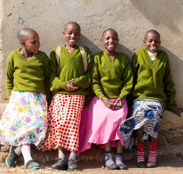 Four Tanzanian girls standing together wearing green uniform sweaters