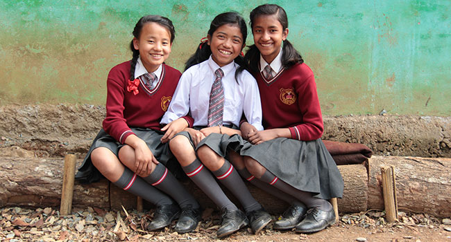 Three girls sitting on bench outside wearing school uniforms
