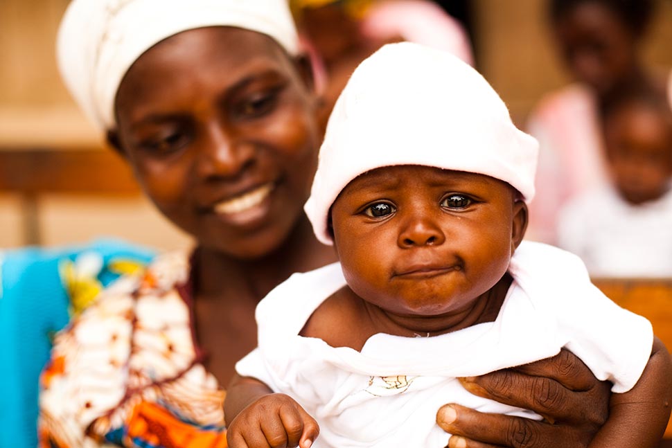 A woman holds up a baby dressed in white