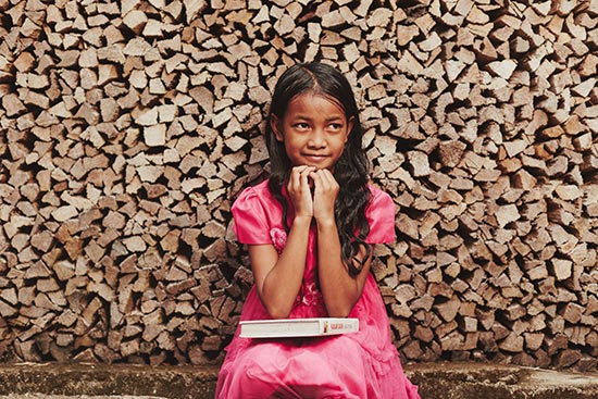 A girl in a pink dress sitting in front of a stack of wood