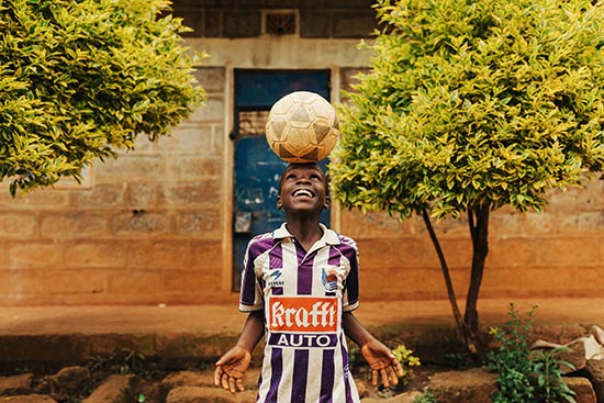 A boy in a soccer jersey balances a soccer ball on his head