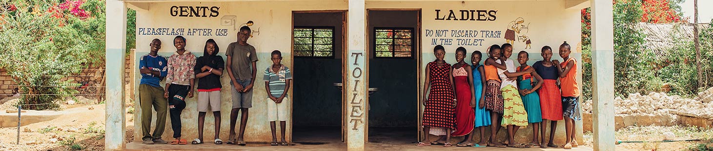 a group of young men and young women stand in front of a building with men's and women's hygienic toilets