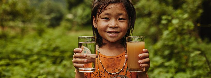A young Thai girls holds up a glass of clean water and a glass of dirty water.