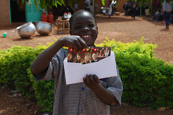 A boy in Burkina Faso opening a letter from his sponsor with pictures inside