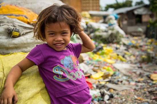 Young girl smiling while standing near trash piles