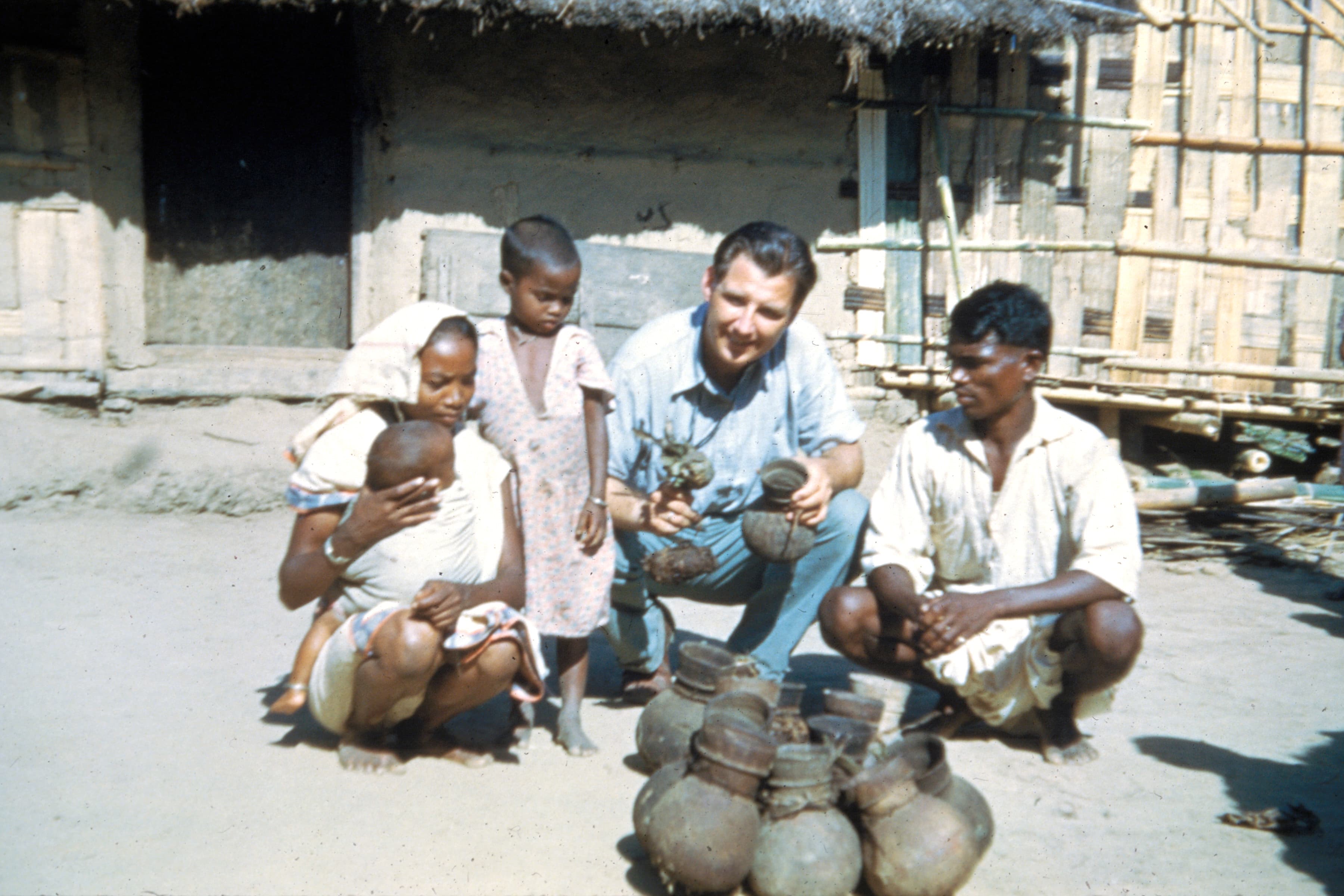 Everett Swanson sits on the ground with a family behind pots.
