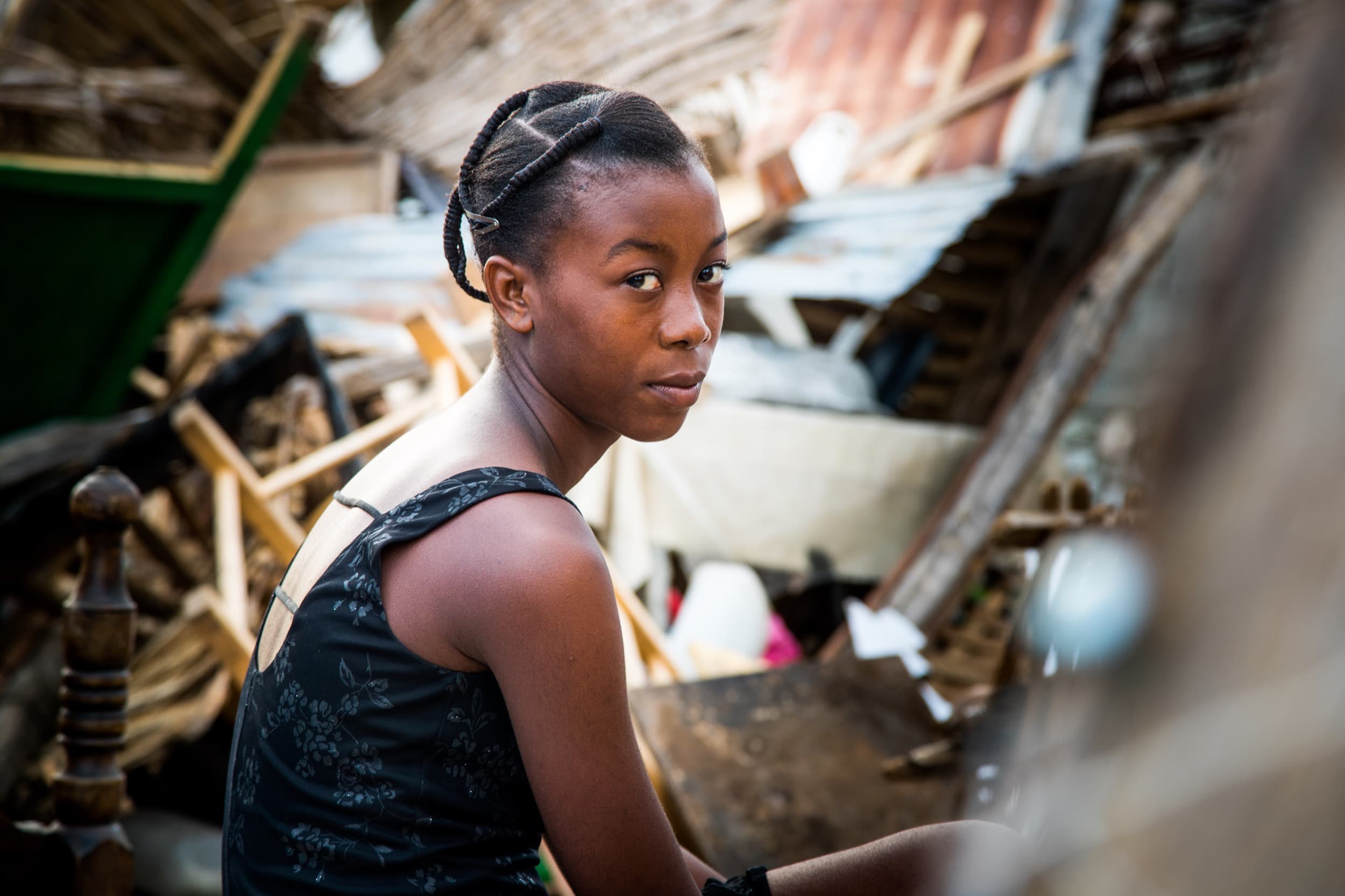 A young woman sits surrounded by wood and other debris.